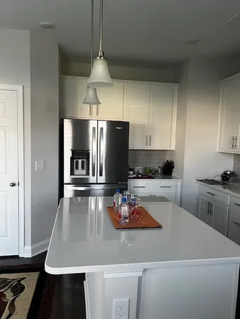 a kitchen with kitchen island granite countertop a refrigerator a stove and white cabinets with wooden floor