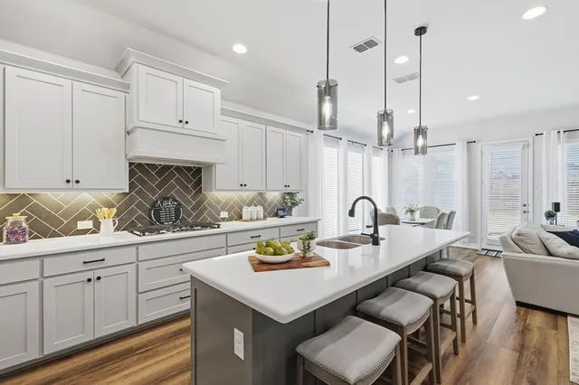 a kitchen with stainless steel appliances granite countertop a sink a stove and white cabinets with wooden floor