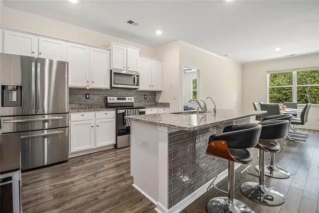 a kitchen with stainless steel appliances granite countertop a stove a sink a refrigerator and white cabinets with wooden floor