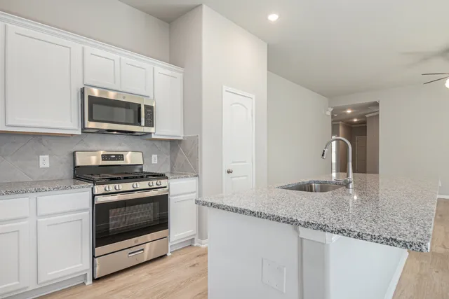 a kitchen with granite countertop a stove a microwave a sink and cabinets