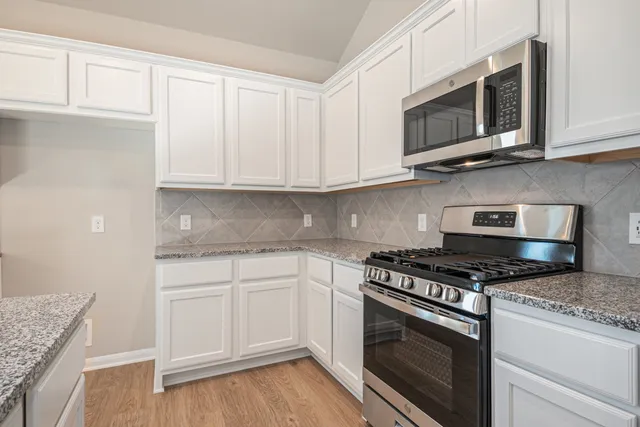 a kitchen with granite countertop white cabinets stainless steel appliances and wooden floor