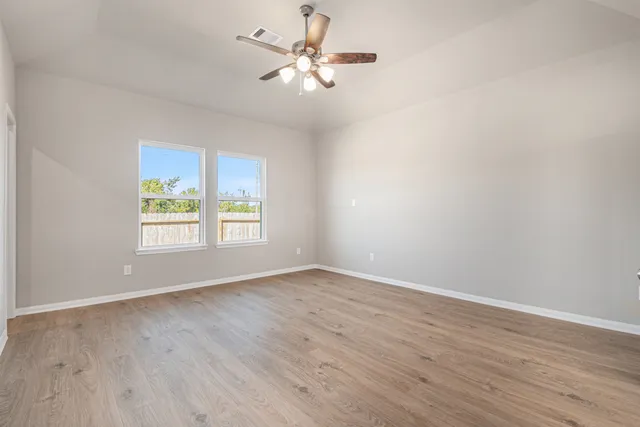 an empty room with wooden floor chandelier fan and windows