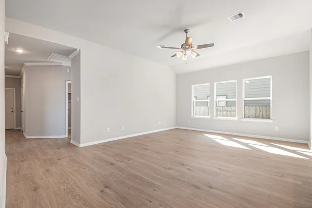 an empty room with wooden floor ceiling fan and windows
