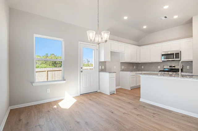 a kitchen with stainless steel appliances granite countertop a refrigerator a sink dishwasher a stove and white cabinets with wooden floor