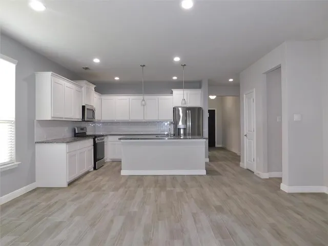 a view of kitchen with granite countertop refrigerator oven sink and white cabinets with wooden floor
