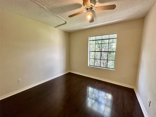 an empty room with wooden floor fan and windows
