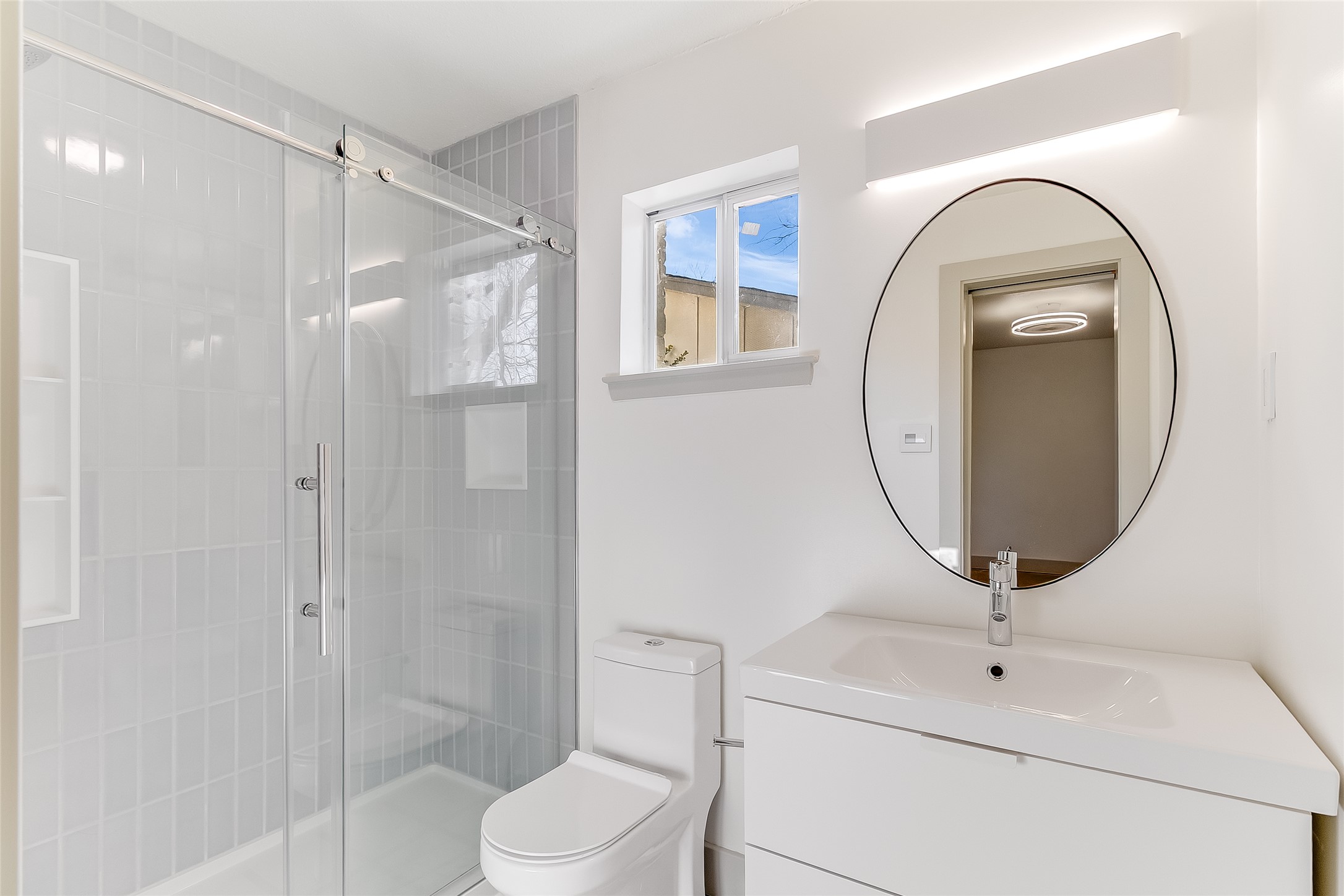 10101 Rutland Village East Austin, TX 78758 - Photo 16 of 26 Primary bathroom with LVP terrazzo tile floor, new toilet, floor to ceiling tile in walk-in shower, polished chrome mirror and window for natural light.