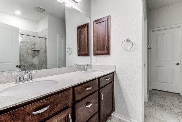 1237 Volente Lane Leander, TX 78641 - Photo 14 of 22 Double vanities with sleek countertops complement rich wooden cabinetry in this well-appointed bathroom.