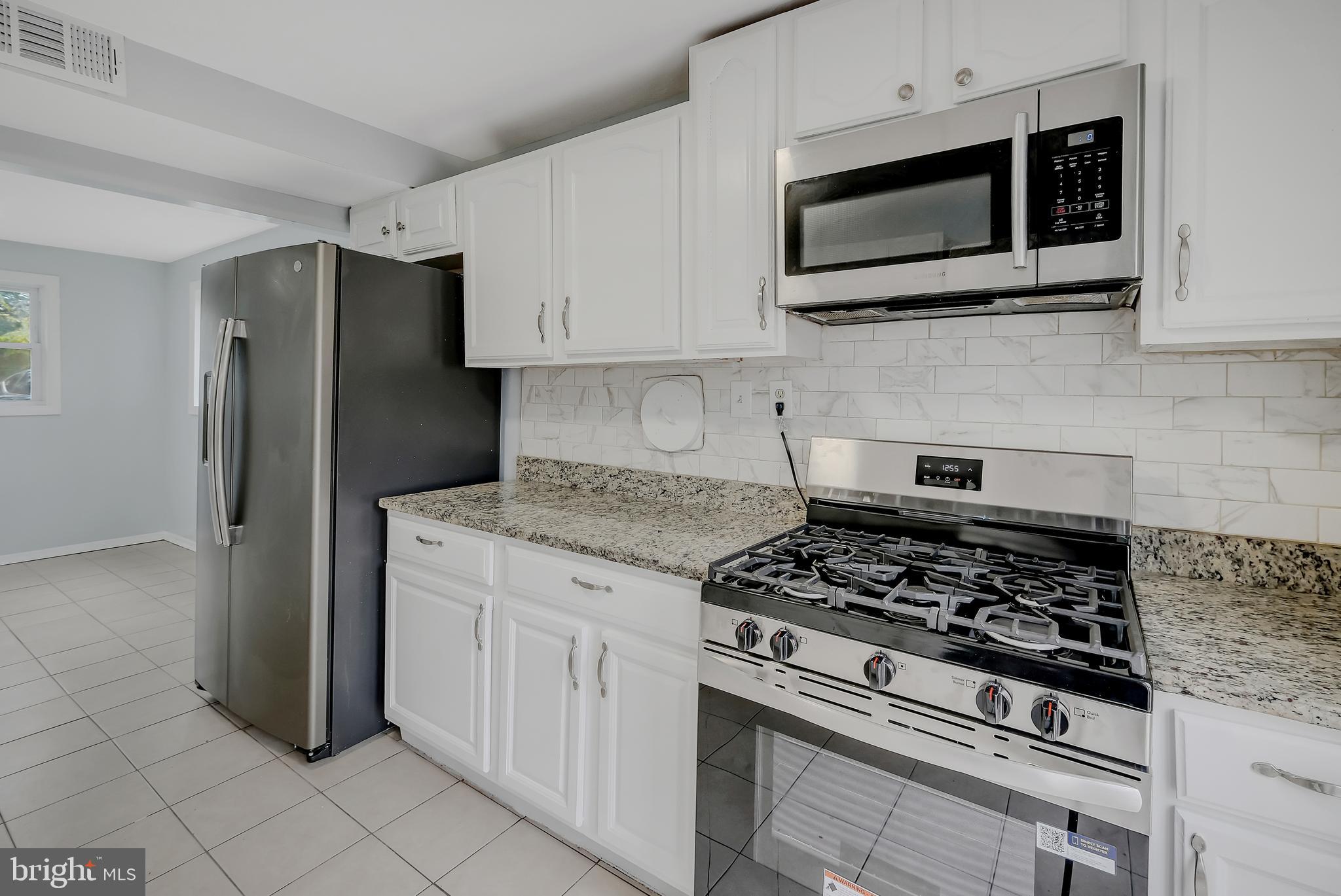 4205 Ferrara Drive Silver Spring, MD 20906 - Photo 8 of 38 a kitchen with stainless steel appliances granite countertop white cabinets a stove a microwave and a refrigerator