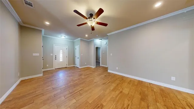 a view of an empty room with wooden floor and a ceiling fan