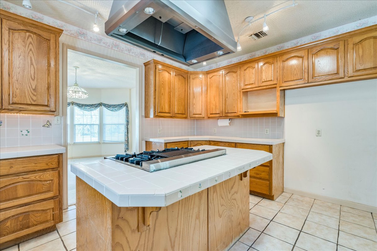 19106 Eyerley Road Manor, TX 78653 - Photo 11 of 40 A well-equipped kitchen boasts a central island cooktop, plentiful wood cabinetry, and tiled surfaces.