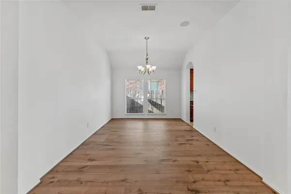 a view of an empty room with chandelier and wooden floor