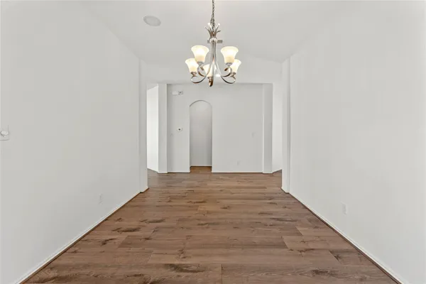 a view of an empty room with chandelier and wooden floor