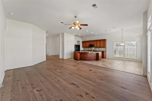 an empty room with wooden floor a ceiling fan window and a kitchen view