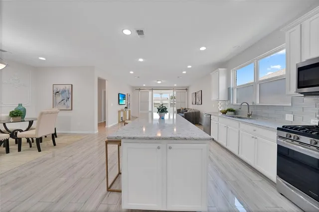 a kitchen with stainless steel appliances kitchen island granite countertop a stove a sink a dining table and chairs