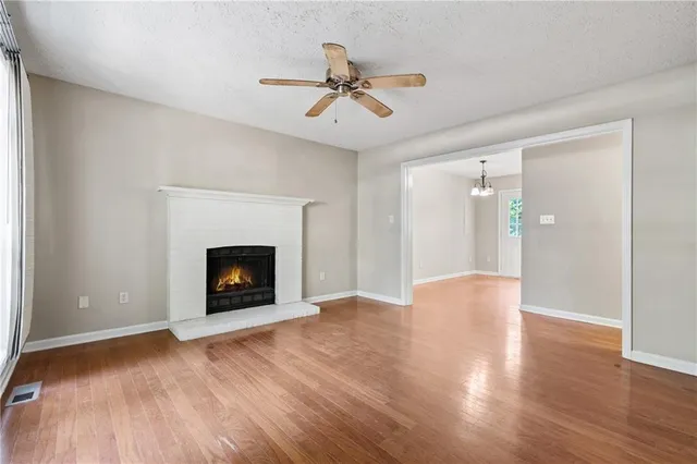 a view of an empty room with wooden floor fireplace and a window