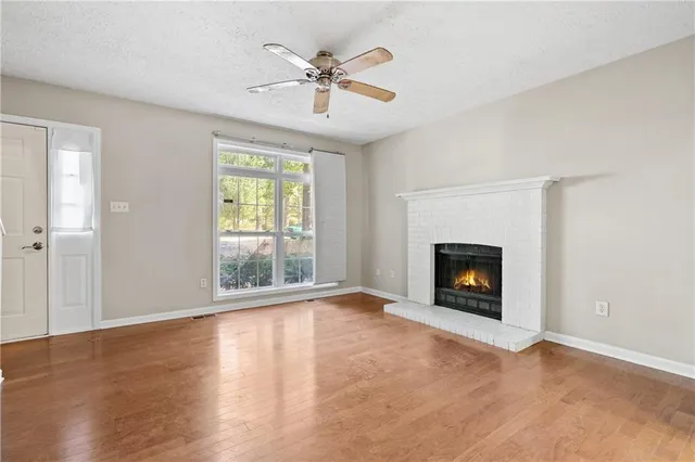 an empty room with windows a fireplace a ceiling fan and wooden floor