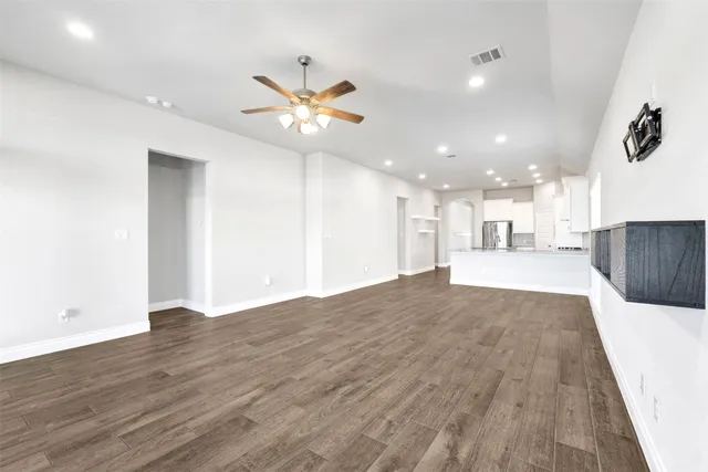 a view of an empty room and kitchen with wooden floor