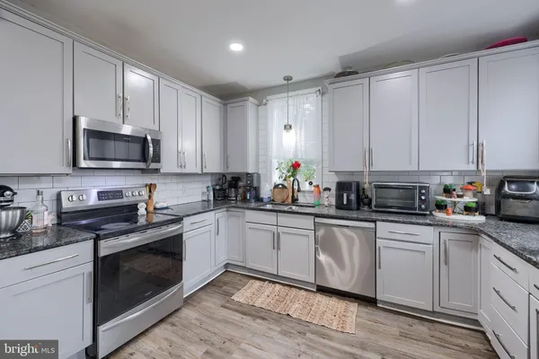 a white kitchen with granite countertop white cabinets stainless steel appliances and a sink