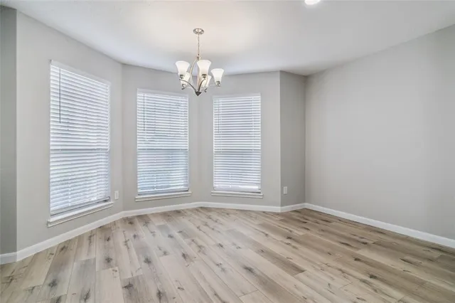 an empty room with wooden floor chandelier and windows