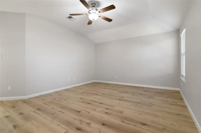 an empty room with wooden floor fan and windows