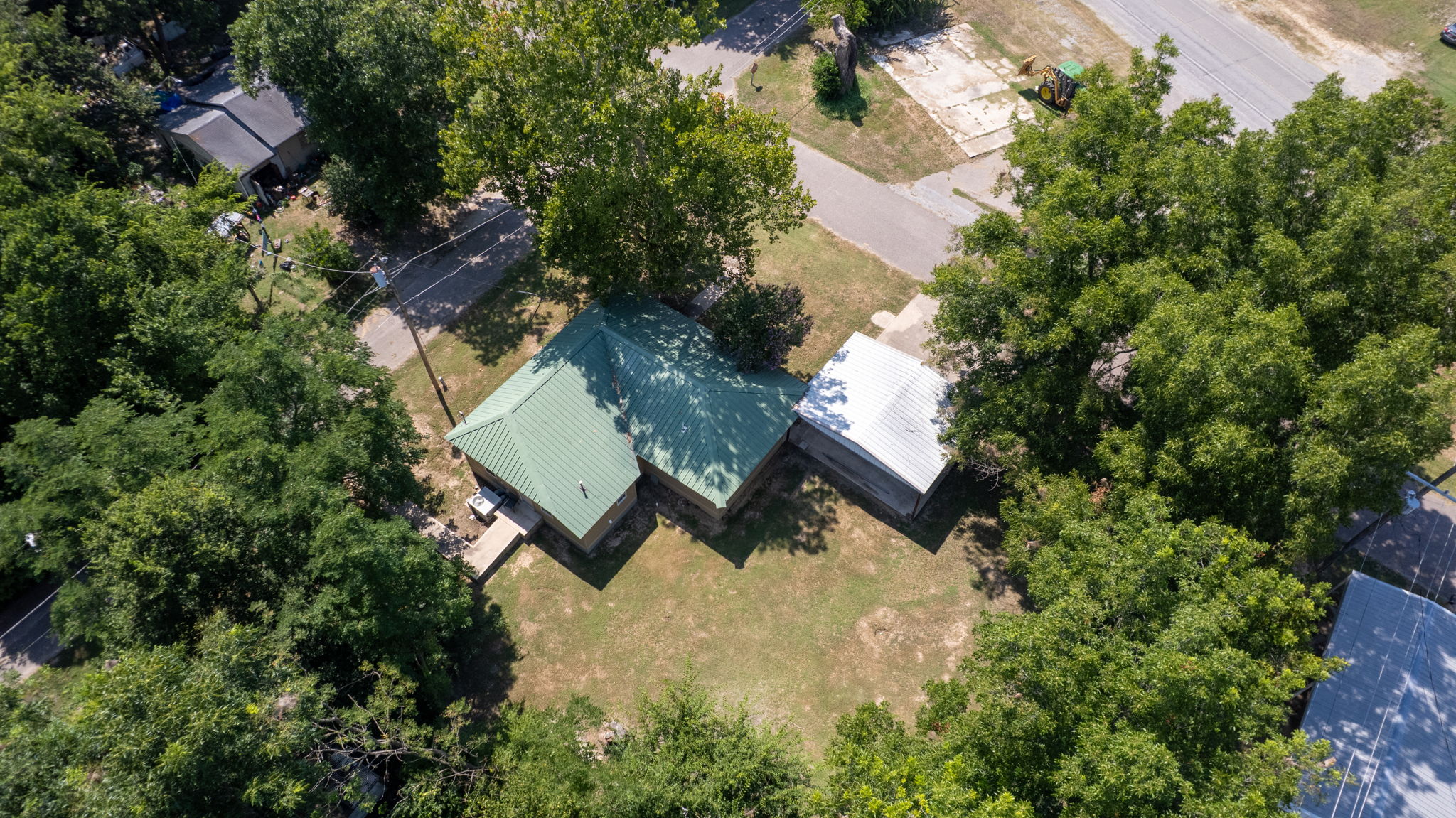 210 Main Caddo, OK 74729 - Photo 26 of 30 Residential property with a green metal roof and a light-colored metal roof section, surrounded by mature trees