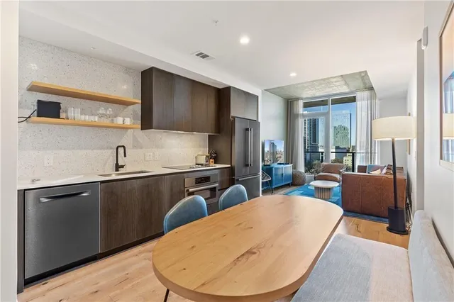 a kitchen with stainless steel appliances granite countertop a sink dishwasher a refrigerator and couches with wooden floor