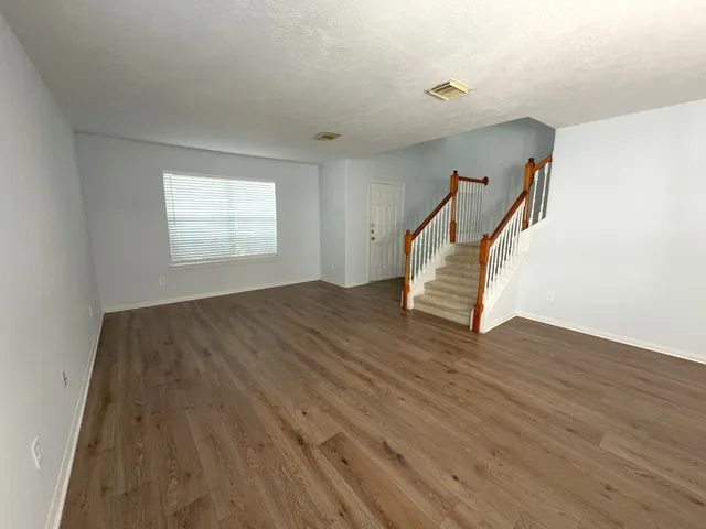 a view of an empty room with wooden floor and stairs