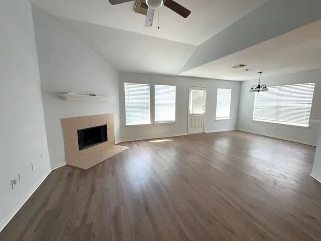 an empty room with wooden floor fireplace and windows