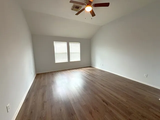 an empty room with wooden floor chandelier fan and windows