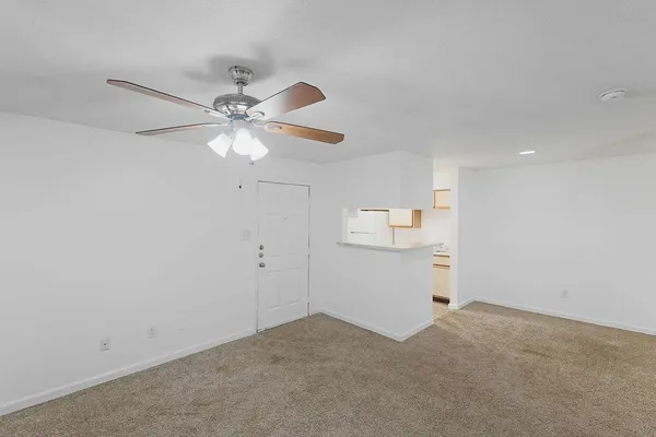 an empty room with chandelier fan and kitchen view