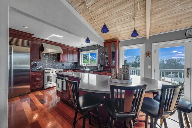 a kitchen with stainless steel appliances granite countertop a stove a refrigerator a kitchen island a dining table and chairs with wooden floor