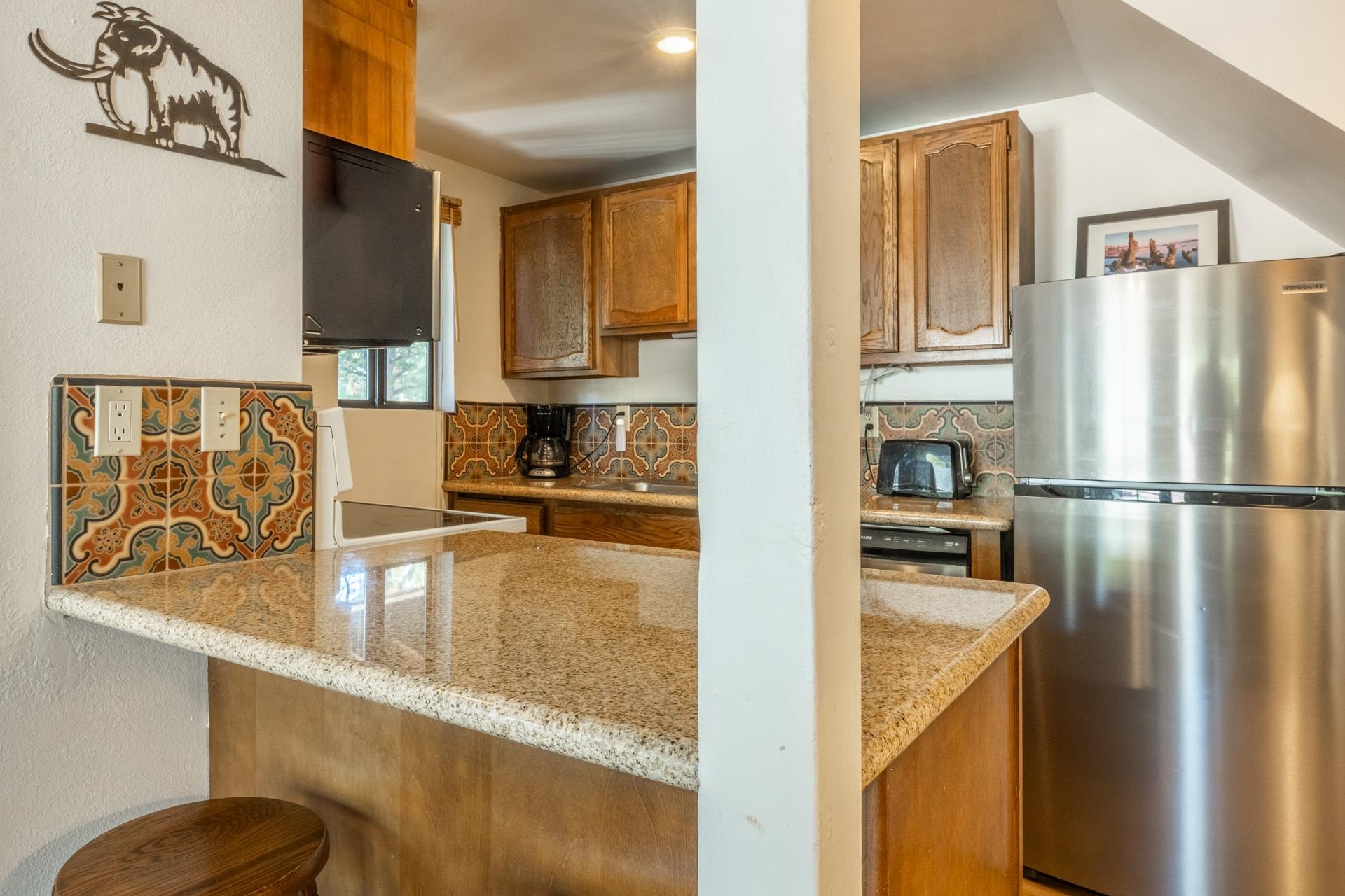 153 Lake Mary Road, Unit 132 Mammoth Lakes, CA 93546 - Photo 7 of 20 Kitchen featuring freestanding refrigerator, brown cabinets, light stone countertops, and a textured wall