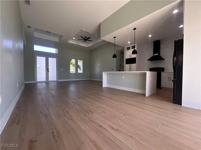 a view of an empty room with wooden floor and a kitchen