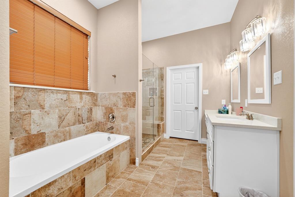 5230 Esquire Estates Road Mabank, TX 75156 - Photo 20 of 39 Bathroom featuring a built-in soaking tub with stone tile surround, a glass-enclosed shower, dual vanity with white cabinetry and integrated sinks, and coordinating stone tile flooring