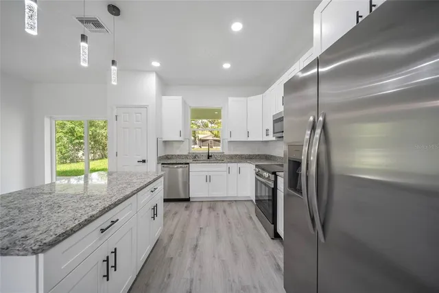 a white kitchen with granite countertop a sink a counter top stainless steel appliances and cabinets