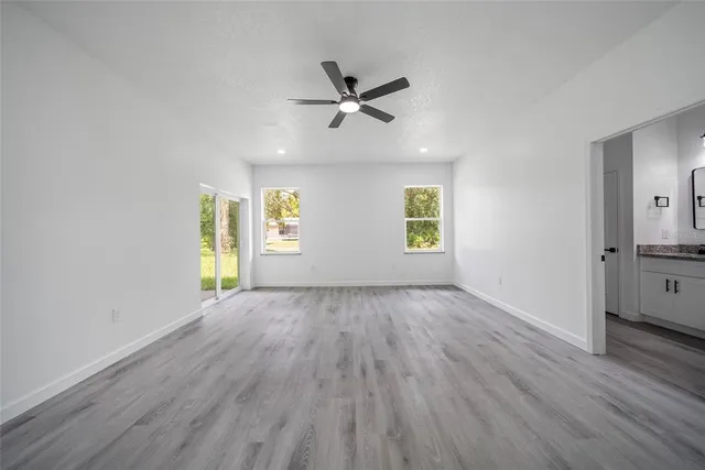 an empty room with wooden floor a ceiling fan and windows