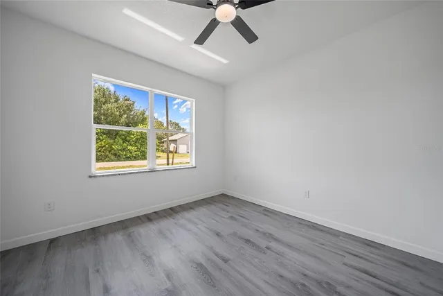 an empty room with wooden floor ceiling fan and windows