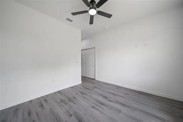 an empty room with wooden floor ceiling fan and windows