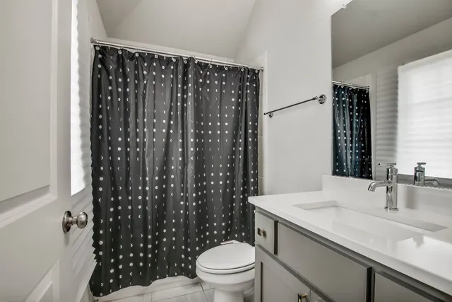 a bathroom with a granite countertop sink a toilet a mirror and shower curtain