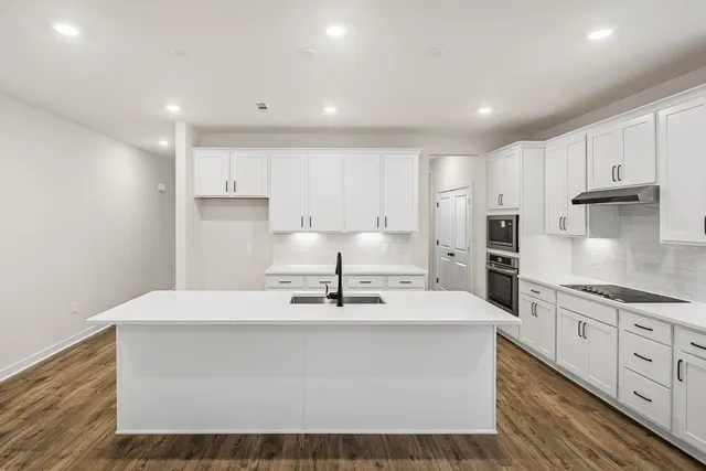 a large white kitchen with kitchen island a sink stainless steel appliances and cabinets