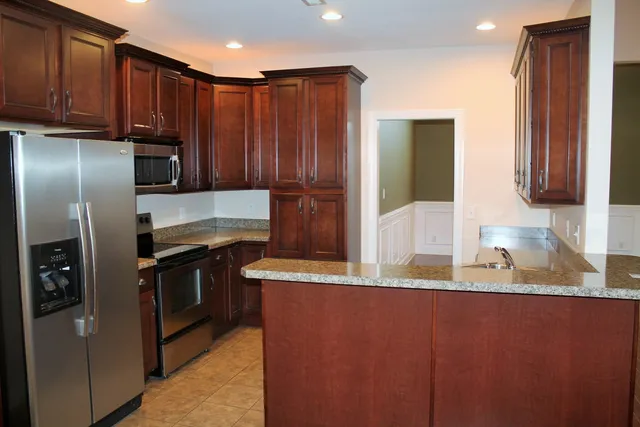 a kitchen with stainless steel appliances granite countertop a refrigerator a stove and a sink with wooden cabinets