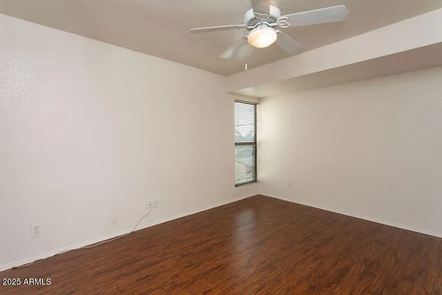 an empty room with wooden floor fan and windows