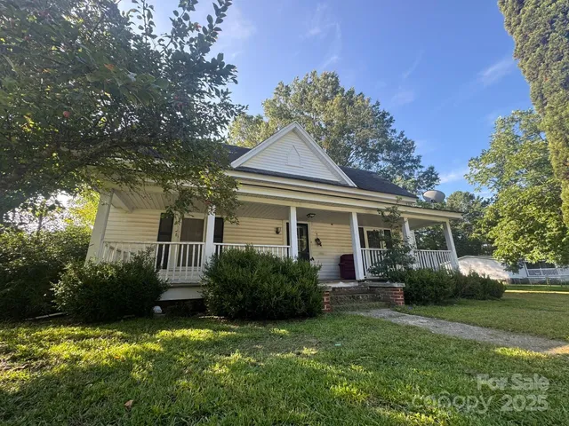 a view of a house with a big yard and potted plants and large trees