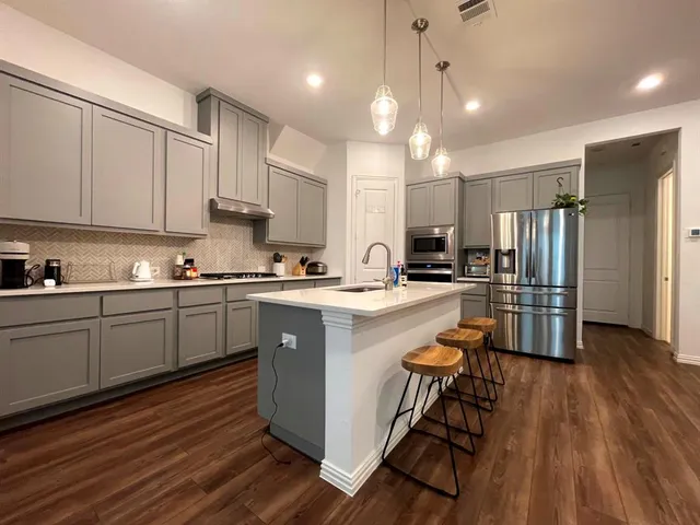a kitchen with stainless steel appliances granite countertop a sink a stove a refrigerator and island with wooden floor