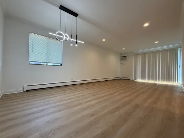 an empty room with wooden floor chandelier fan and windows