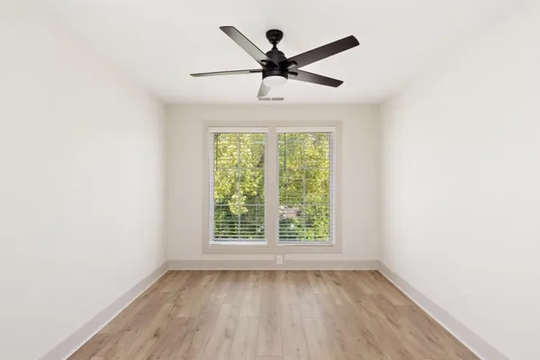 an empty room with wooden floor fan and windows