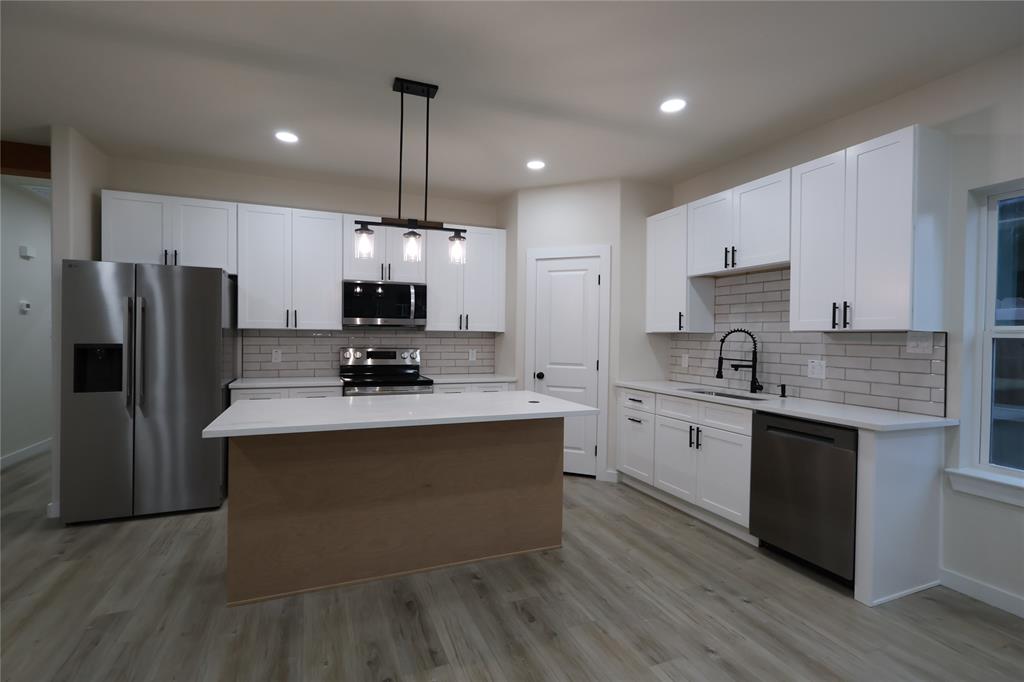 106 Ute Trail Mabank, TX 75156 - Photo 4 of 28 Kitchen featuring appliances with stainless steel finishes, a center island, white cabinets, hanging light fixtures, and light wood-style flooring