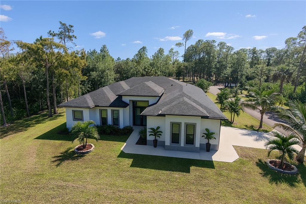 2330 4th Avenue Southeast Naples, FL 34117 - Photo 1 of 39 Rear view of property featuring stucco siding, a lawn, and roof with shingles