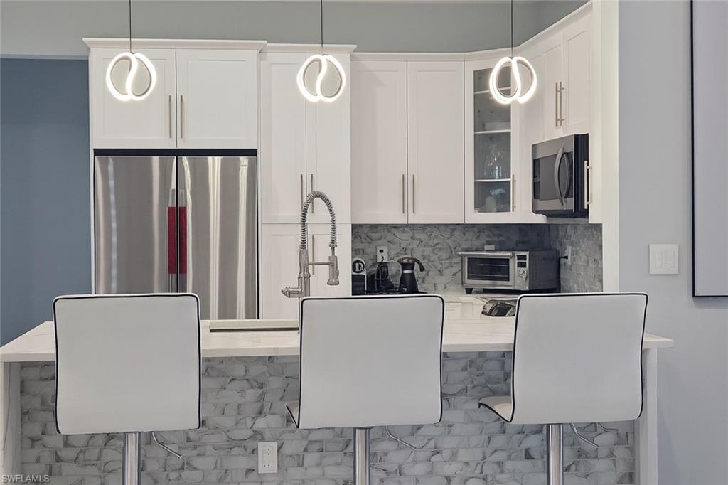 2330 4th Avenue Southeast Naples, FL 34117 - Photo 16 of 39 Kitchen featuring a breakfast bar, white cabinetry, glass insert cabinets, appliances with stainless steel finishes, and backsplash